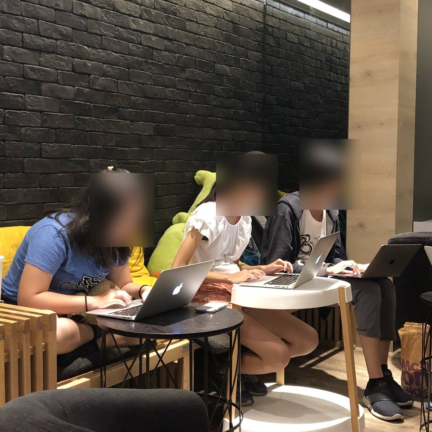 三個孩子在青旅並排坐著,各自對著筆電工作,臉部已模糊處理。
