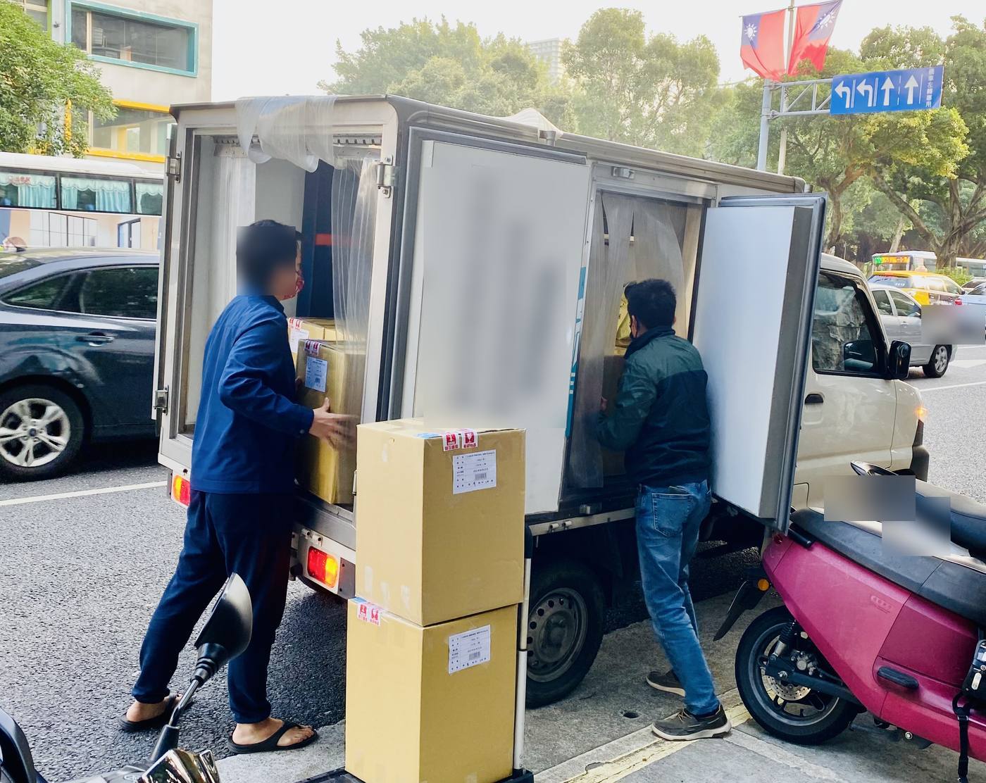 清晨的接貨現場:冷藏車開著門,紙箱堆在人行道上,兩個人正在搬貨。